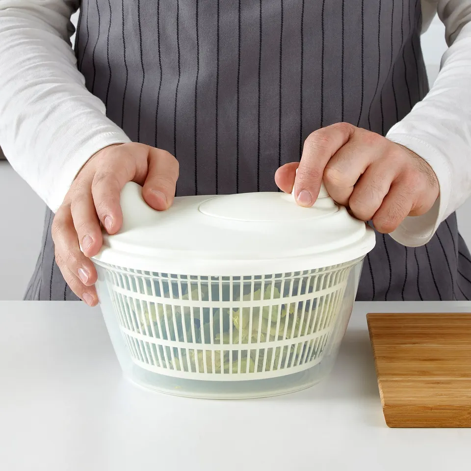 Person holding a salad spinner, placing the lid on it.
