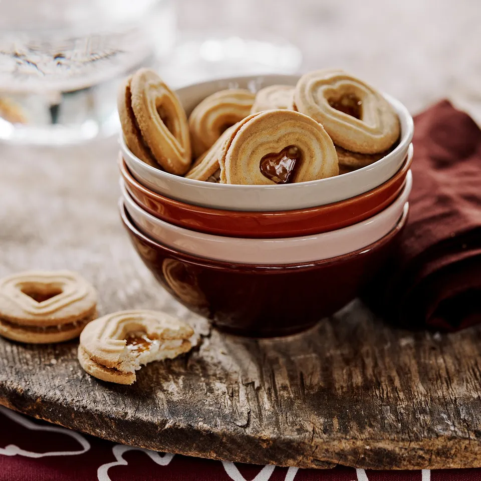Stacked red-brown HÖSTAGILLE bowls with heart-shaped cookies on rustic wood table.
