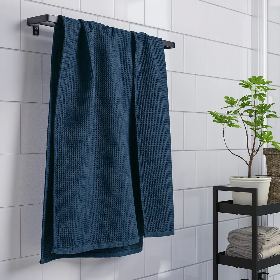 Blue towel on rack with plant and folded towels.