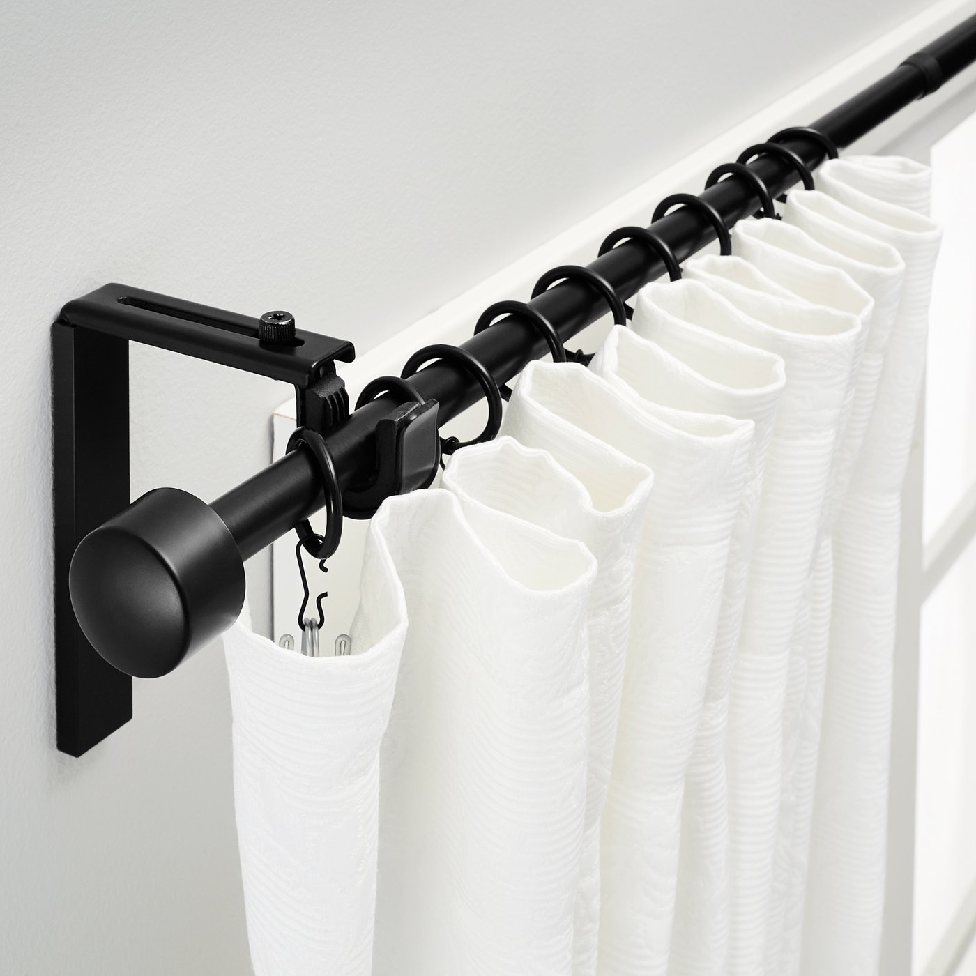 Black curtain rod on wall with white curtains, adjustable length and angle.