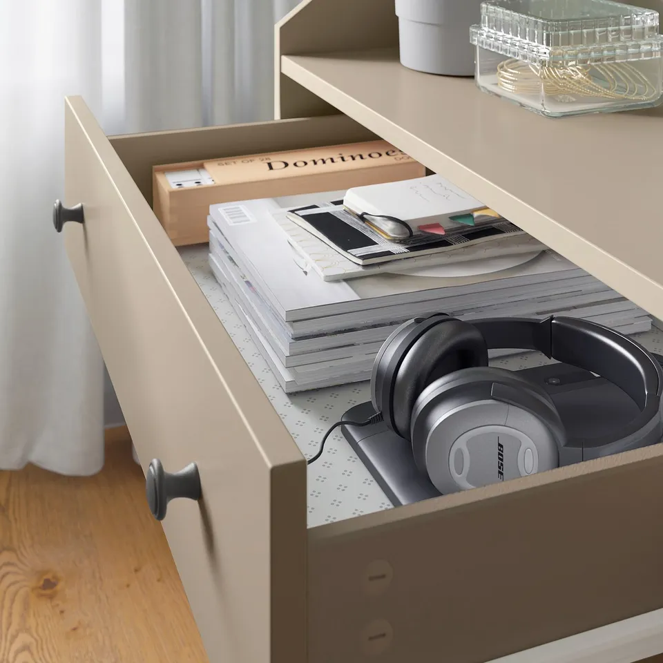 Open beige HAUGA drawer revealing headphones, papers, and a box.