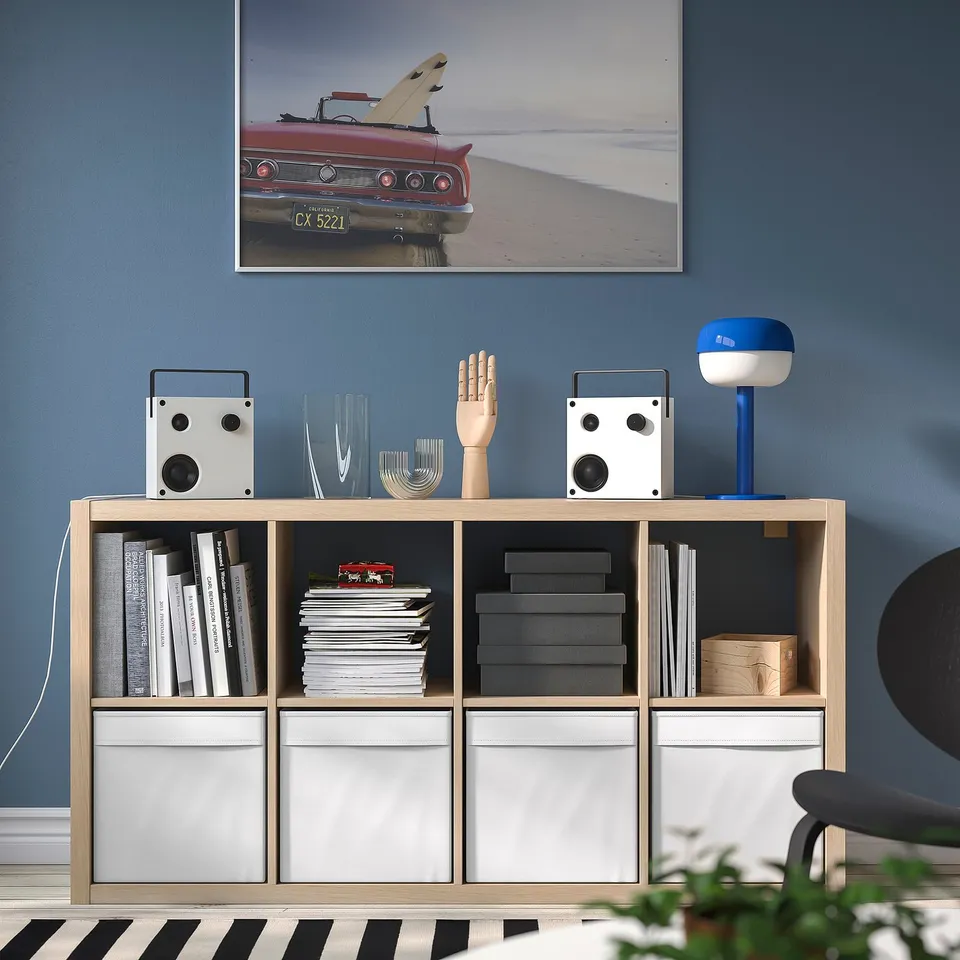 Minimalist living room: blue wall, vintage car photo, bookshelf, VAPPEBY speakers, lamp, sculpture, vase.