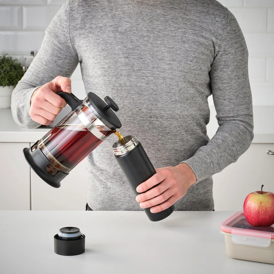 Pouring coffee into travel mug on counter with apple & plant.