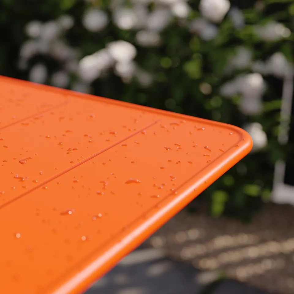 Bright orange, foldable outdoor table with water droplets, set outdoors amidst green foliage.