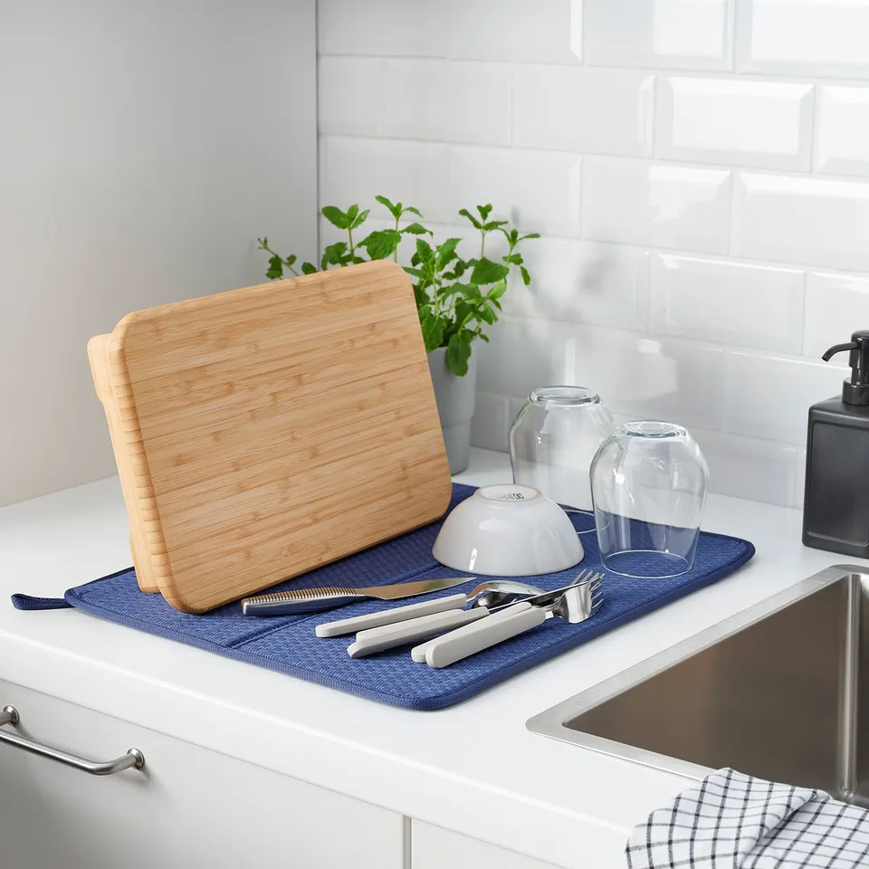 Kitchen counter with wooden cutting board, knives, and blue mat near sink. Also includes vases and soap dispenser.