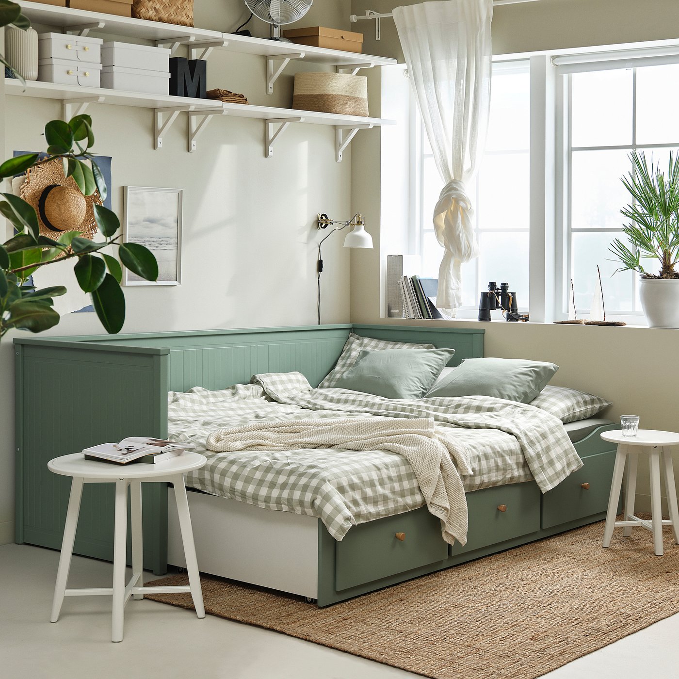 Grey-green HEMNES day-bed with storage, turns into a double bed. Styled with plaid bedding in a room with white shelves.