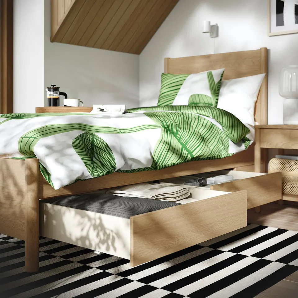 Bed frame with drawers and slatted base, showcasing storage and support. Green and white bedding, coffee by bed.