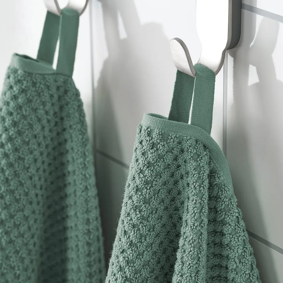 Two green towels hang on hooks, displaying their soft, fluffy texture and sturdy design.