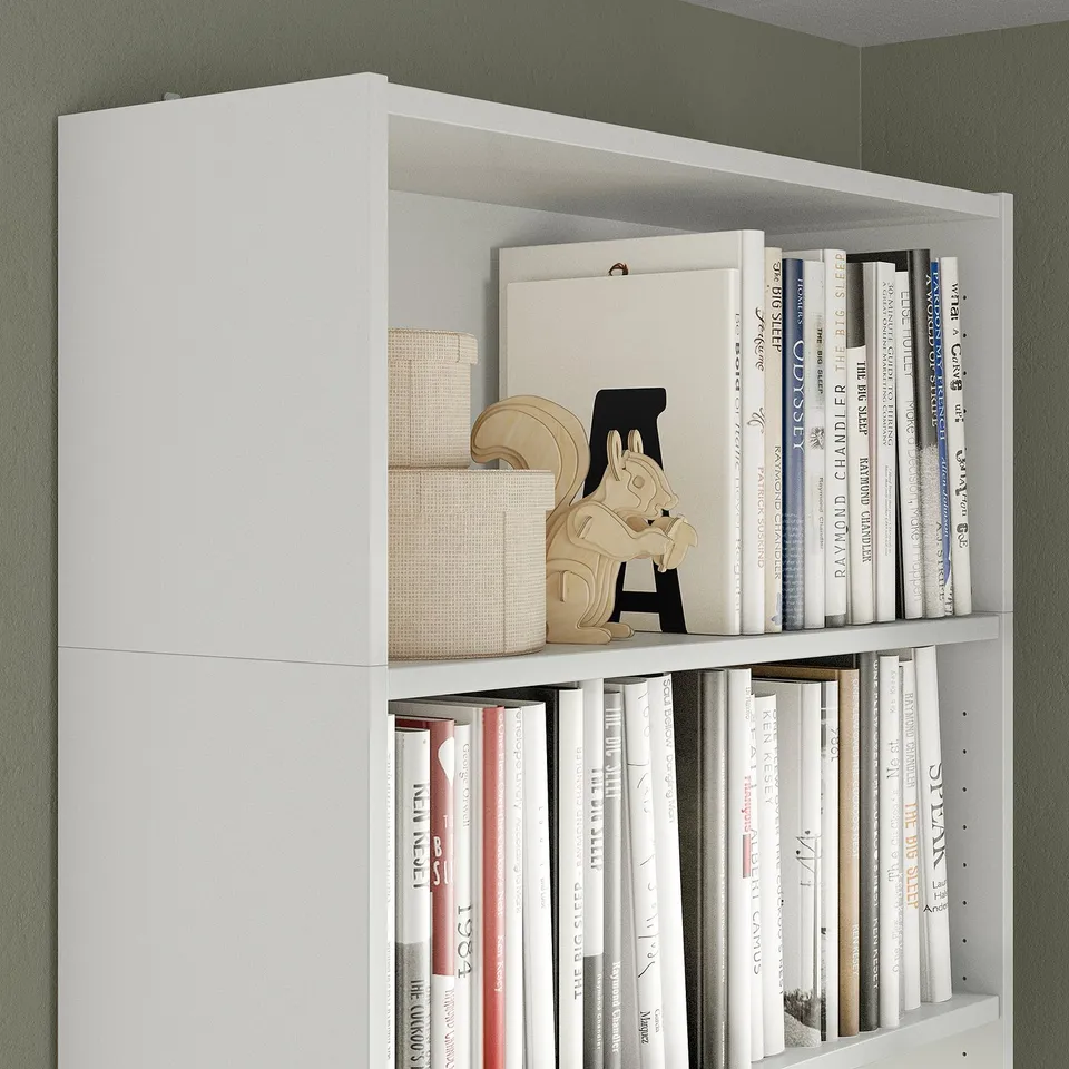 White BILLY bookshelf with adjustable shelves, holding several books and decorative items, including a wooden horse and woven baskets.