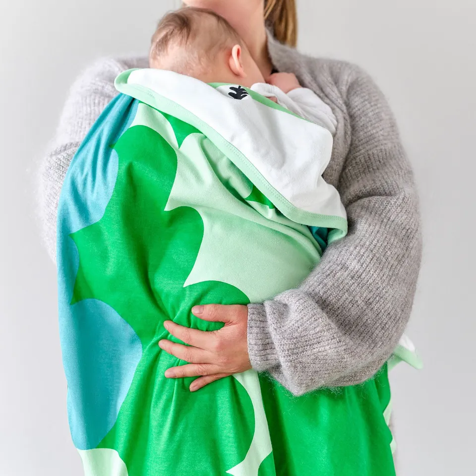A person holding a baby wrapped in a green and white blanket with leaf patterns, ideal for napping and comfort.
