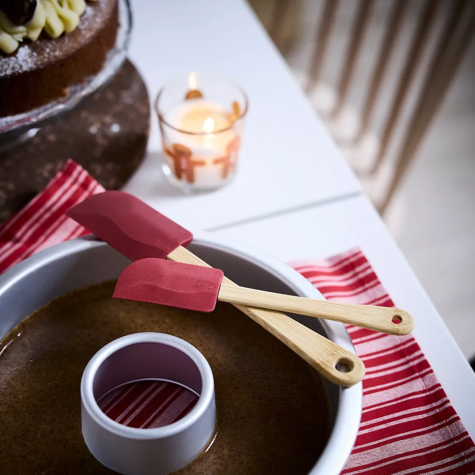 Red VINTERFINT spatulas with bamboo handles, small and easy for kids, sit near mixing bowl and lit candle, striped napkins nearby.