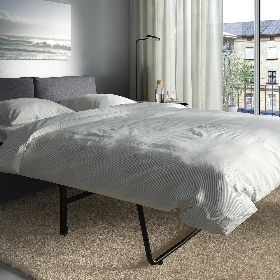 Modern hotel room with VIMLE sofa-bed, white bedspread, large window.