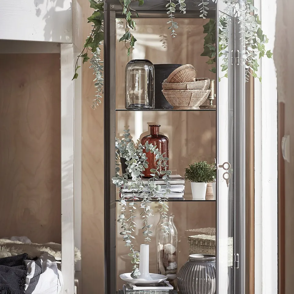 Display cabinet with white renewable eucalyptus plants and decorative baskets.