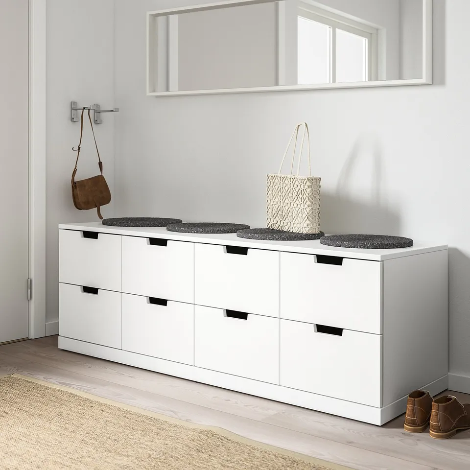 Modern white NORDLI dresser with six drawers. Large, wide, fits under mirror. Dark handles. Small stools and bags on top.
