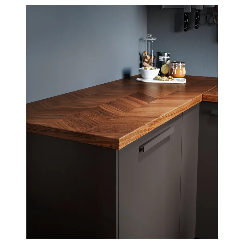 Kitchen counter made of BARKABODA, featuring a dark grey cabinet with a wood-grain patterned top, housing various items like bowls and containers.