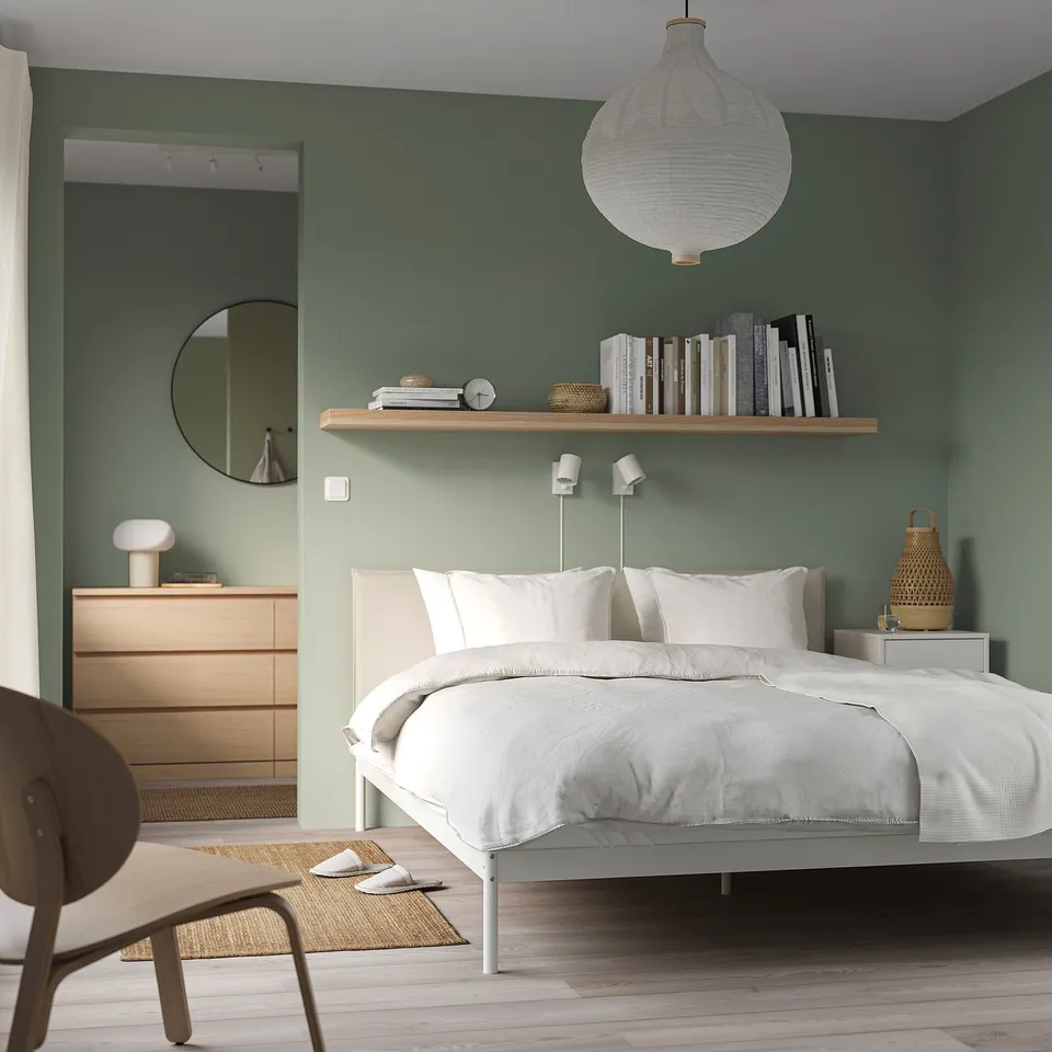 Modern bedroom with green wall, LACK shelf books, white bed, pendant light, dresser, and round mirror.