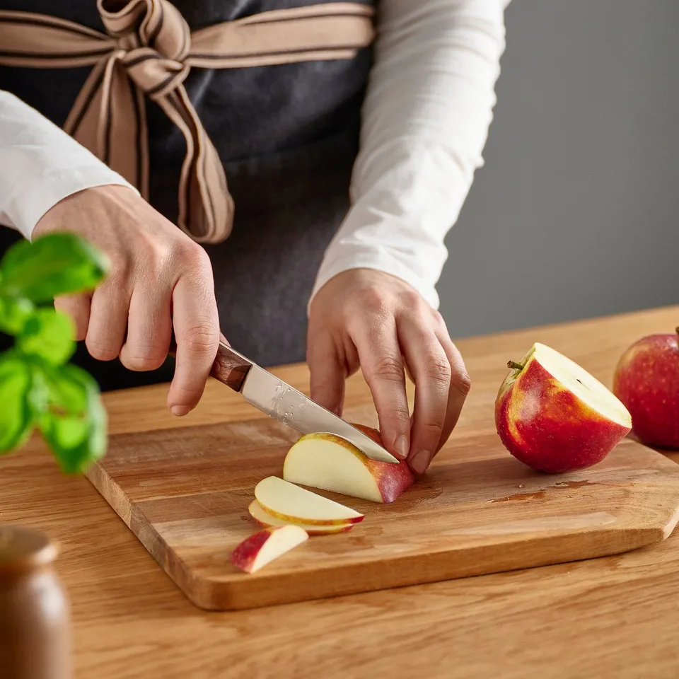 Person slices apple on wooden cutting board using ikea VARDAGEN knife.