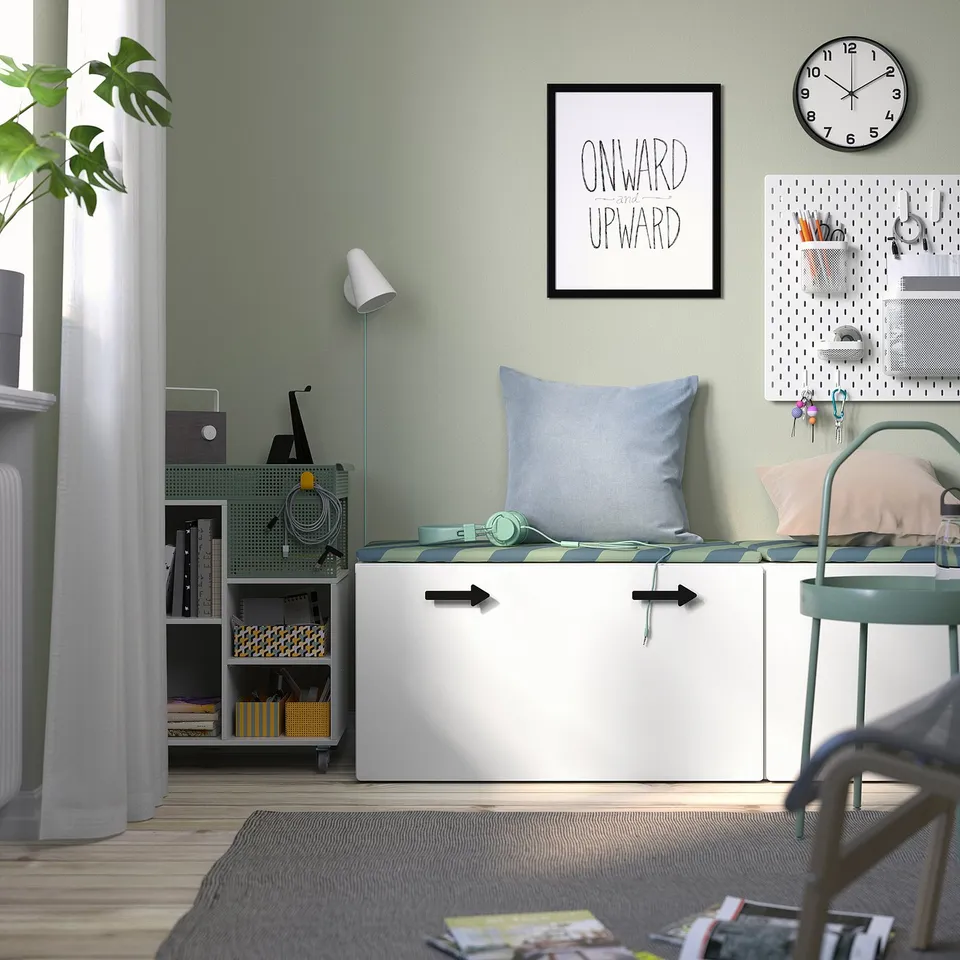 Small white SMÅSTAD storage bench, blue pillow, headphones, neatly organised room with light green walls. Clock and motivational art above.