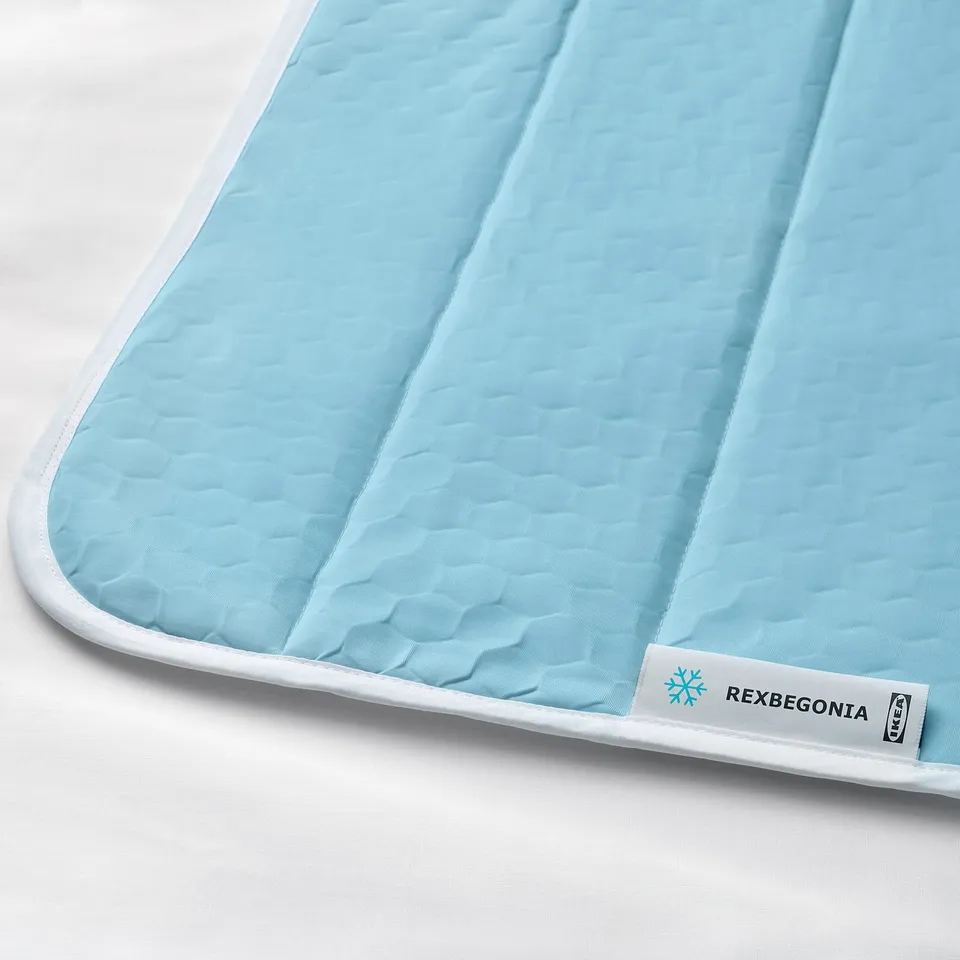 Light blue and white padded cooling mat, neatly folded. High-quality stitching and a tag labelled REXBEGONIA.