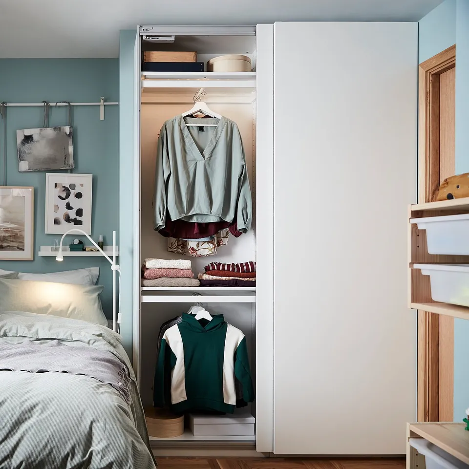 Modern bedroom with white PAX wardrobe, calming blue walls, grey bedding.