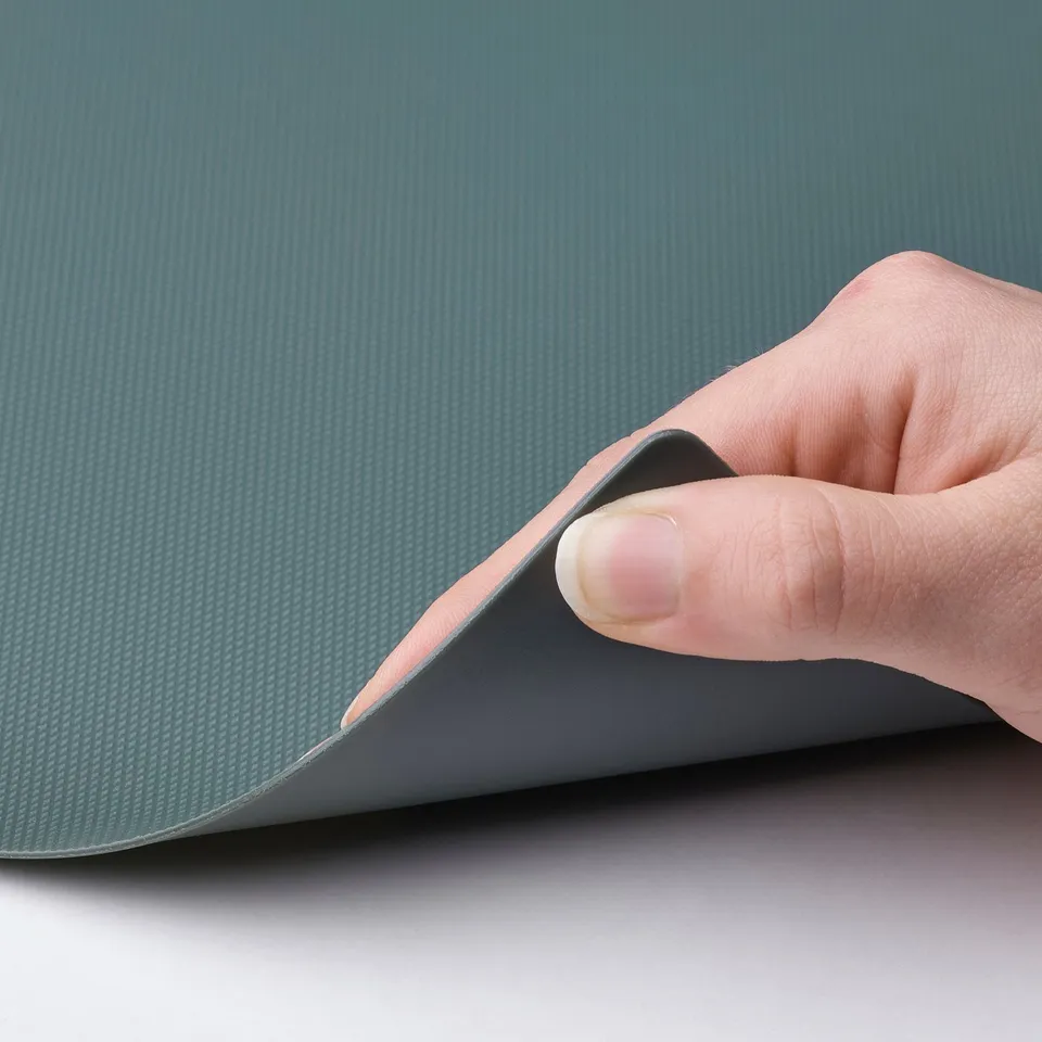 Image shows hand lifting flexible blue-grey chopping board, demonstrating its bendable quality.