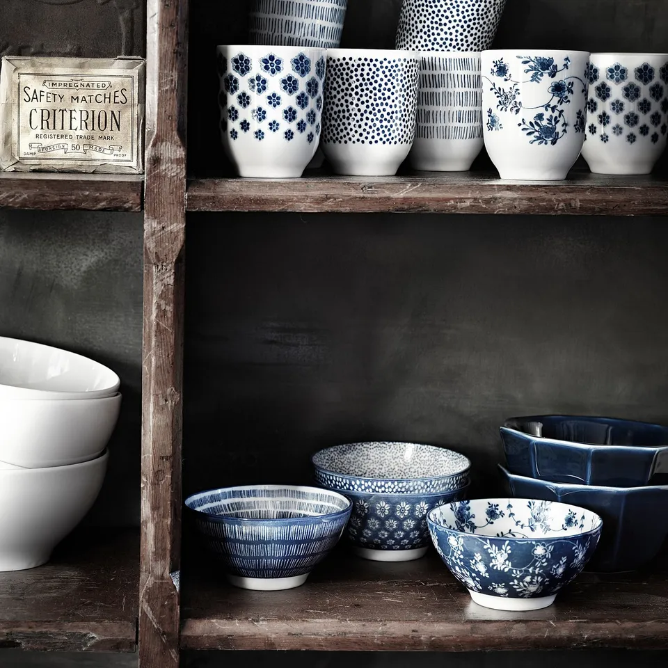 Shelf with blue-white patterned ceramic mugs and bowls; some solid white, varied designs.
