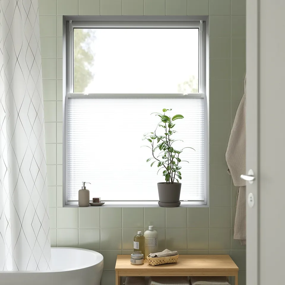 Modern bathroom with light grey HORNVALLMO blinds, plant, and wooden bench with toiletries.