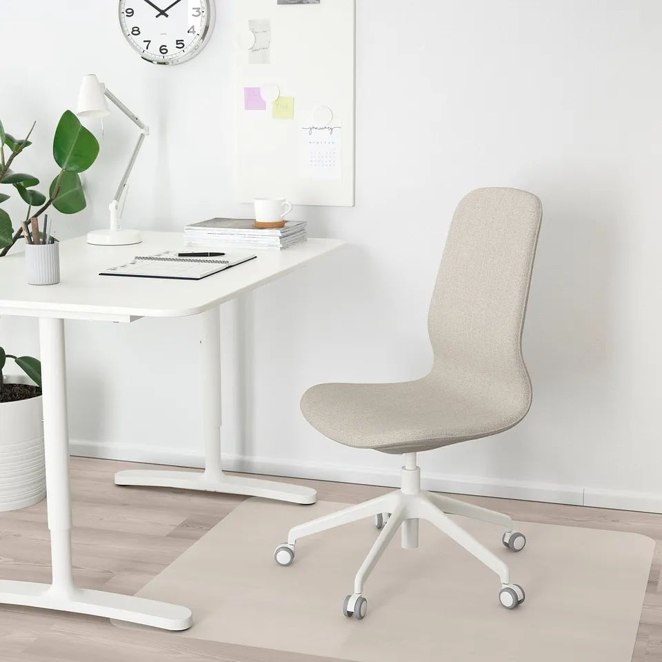 Modern minimalist office setup with white LÅNGFJÄLL chair & desk, light wood flooring, green plant, lamp, & wall clock.