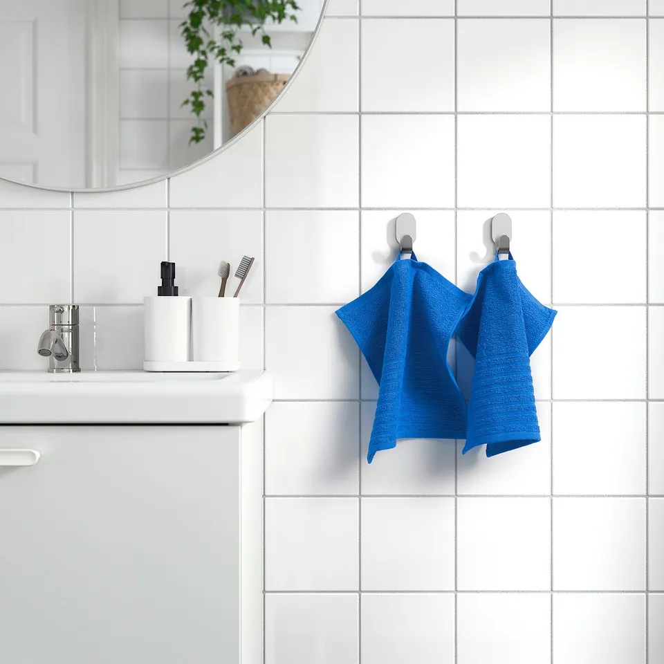 Minimalist bathroom. White tiles, blue towels, silver tap.