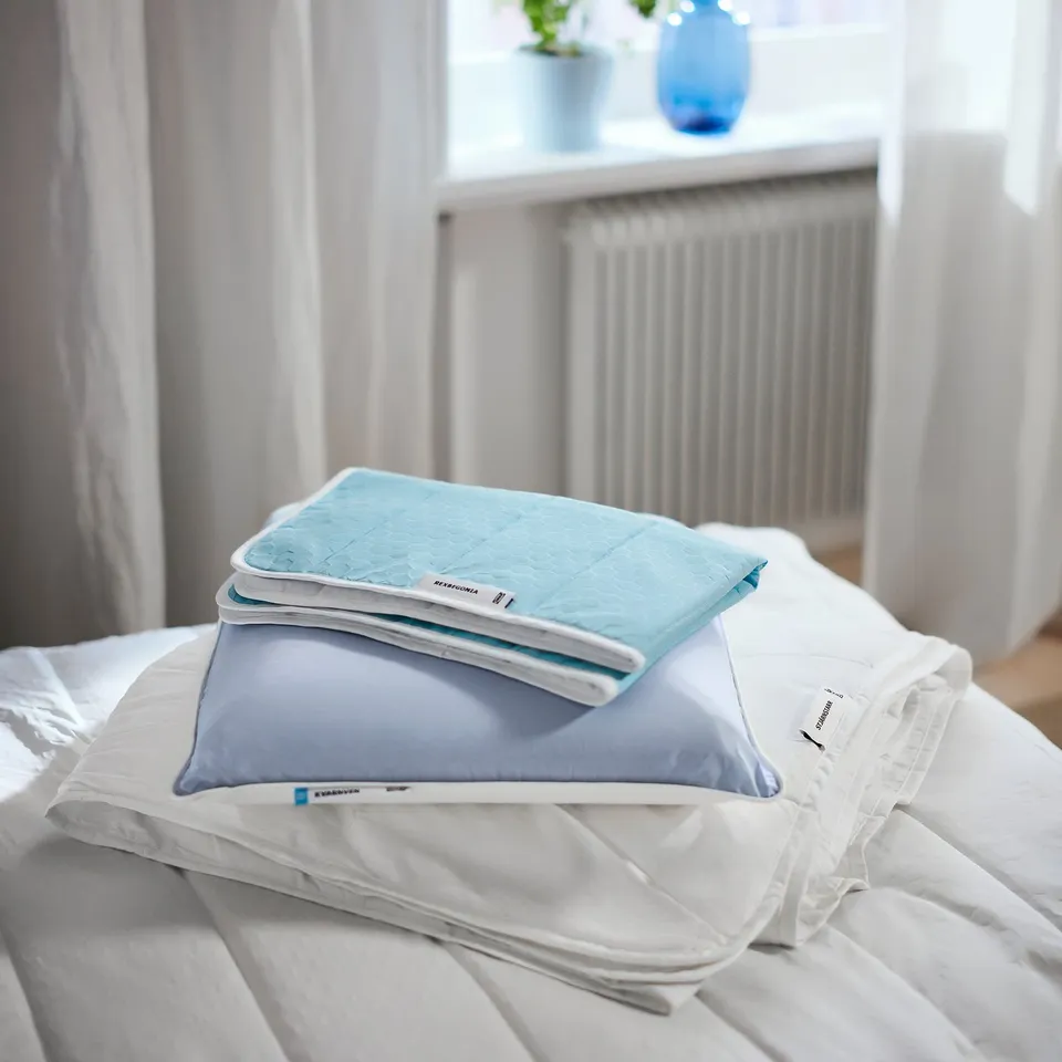Bed with light blue quilted mattress protector, white sheets, and blue pillow, featuring temperature-regulating material.