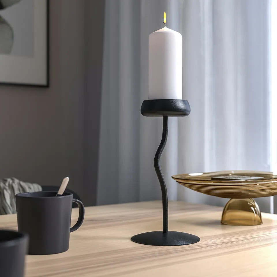 Modern black candlestick with white candle on table, with mug and gold bowl.