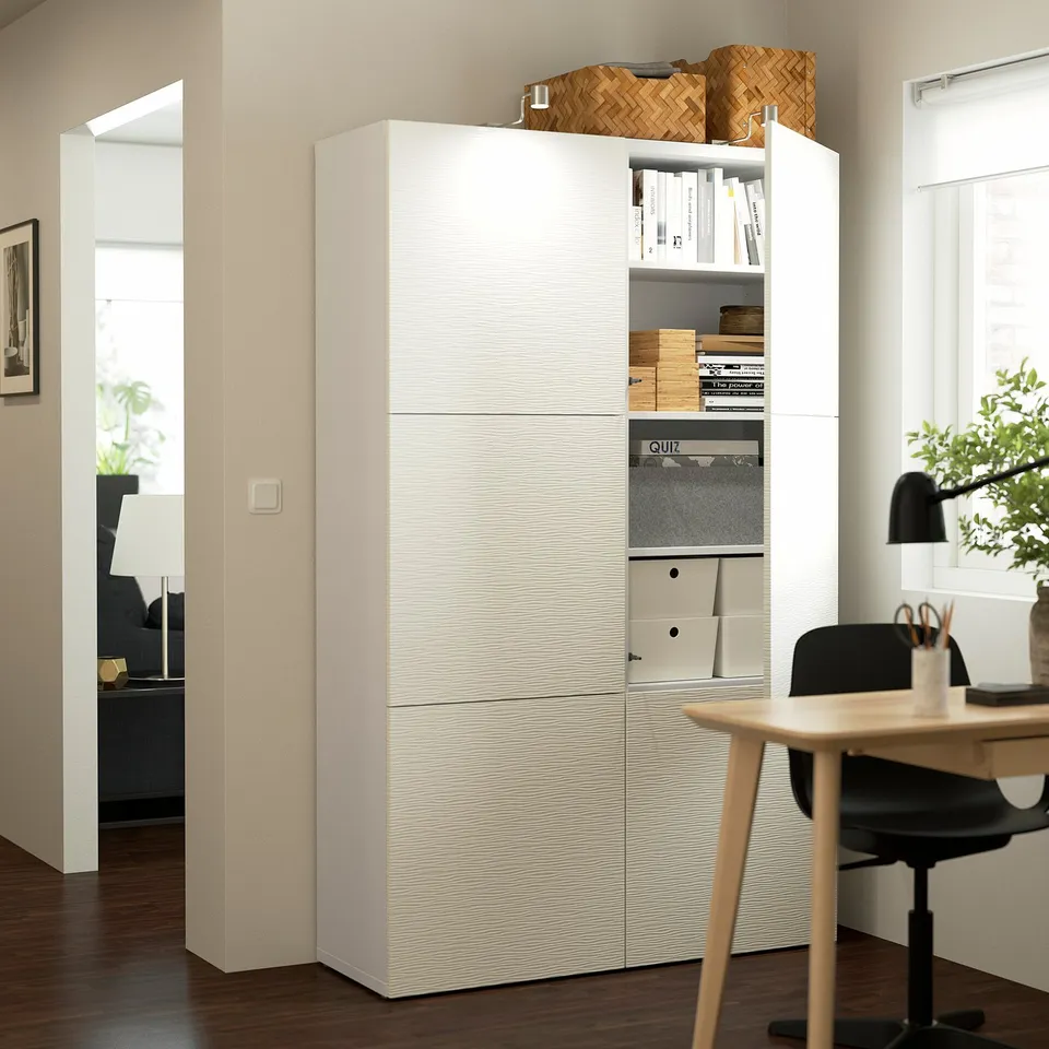 BESTÅ storage unit with shelves and cabinets, displaying books and boxes, next to wooden table and black chair.