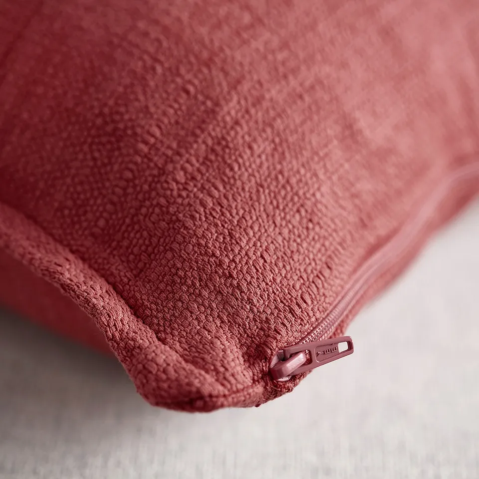 Pink-red cushion with zip and textured surface.