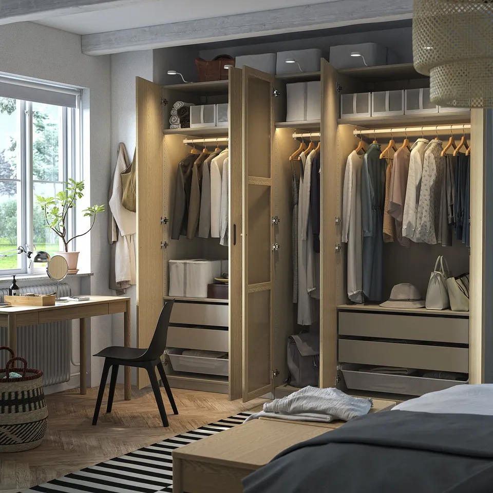 Wooden wardrobe with open doors, clothes, lights. Chair, rug, bed nearby.