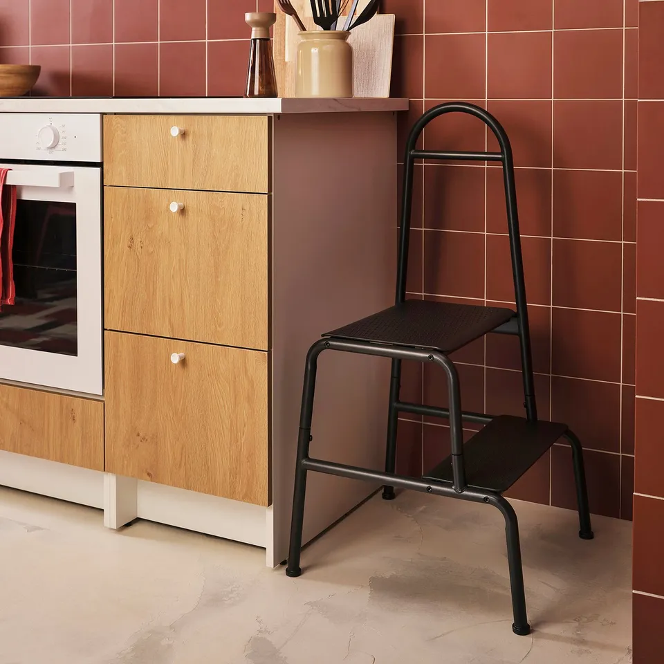 Kitchen with BÄSINGEN 2-step stool, grey metal, wood cabinet, oven, terracotta tiles.
