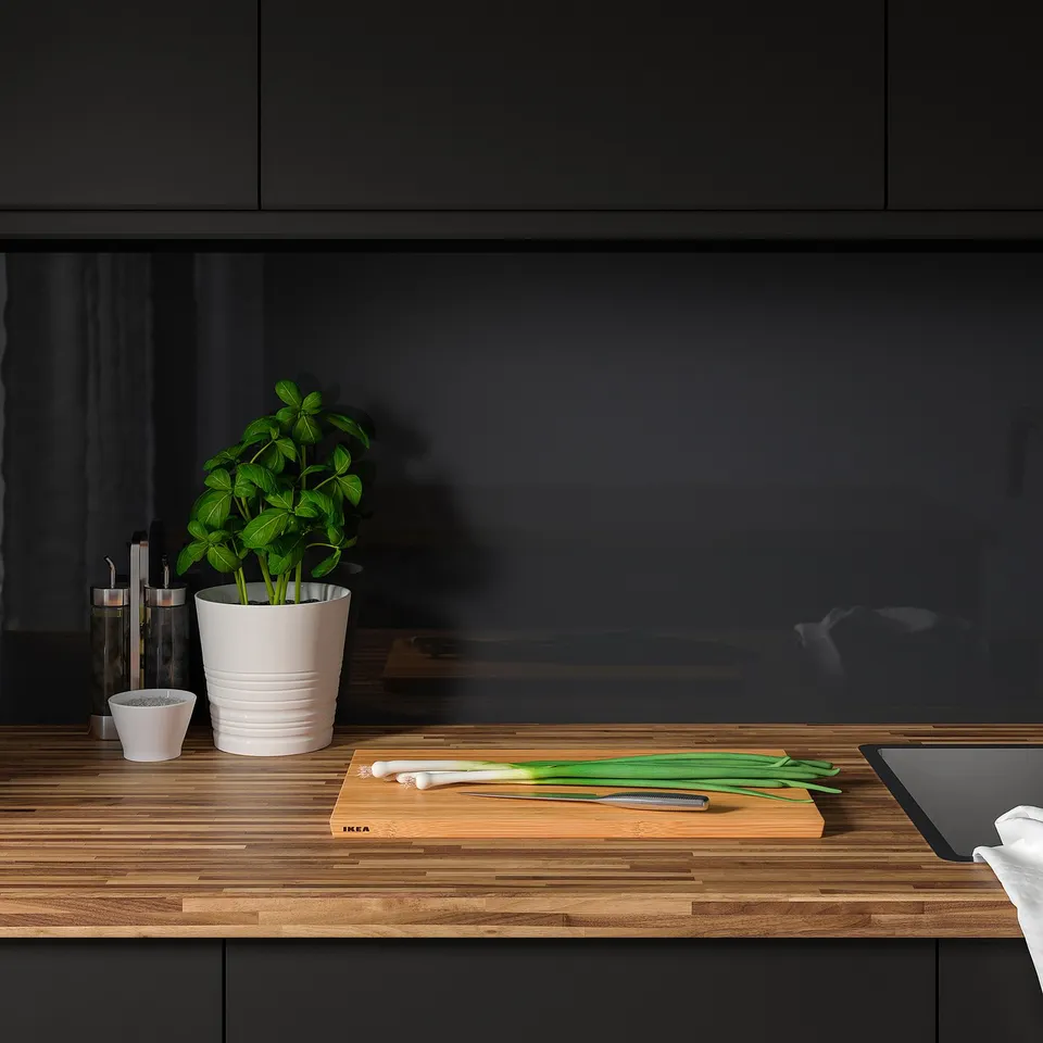 Kitchen counter with cup, plant, scallions, laptop, and knife.