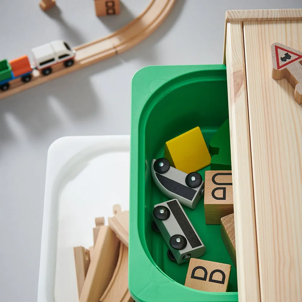 White and green toy storage bin filled with wooden train tracks and accessories.