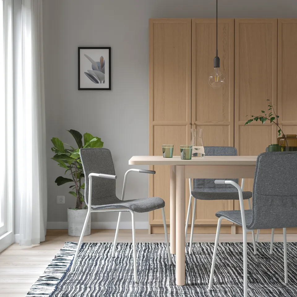 Minimalist dining area with light wood table, grey LÄKTARE chairs, zebra-striped rug, potted plant, and pendant light.