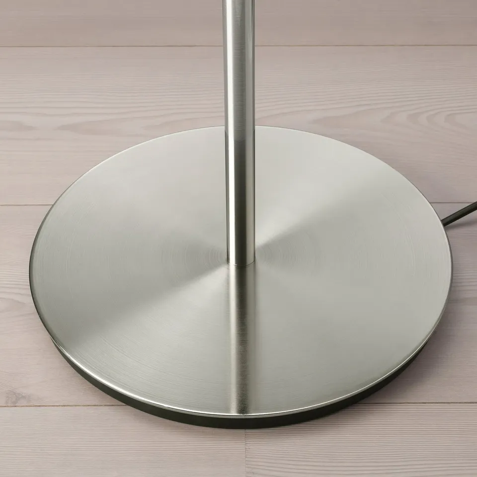 Silver metal base, part of stylish lamp series, sits on wooden floor. Modern design, quality finish.