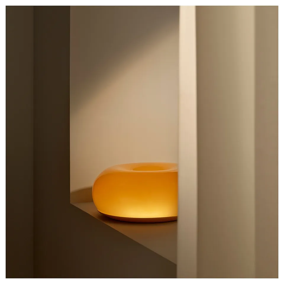 An orange donut-shaped lamp emitting warm light, resting on a shelf between two vertical wooden panels.