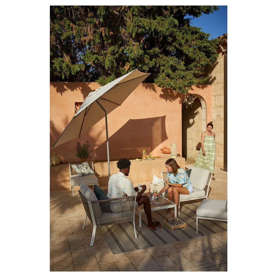 Beige SEGERÖN patio set with couple relaxing, person walking.