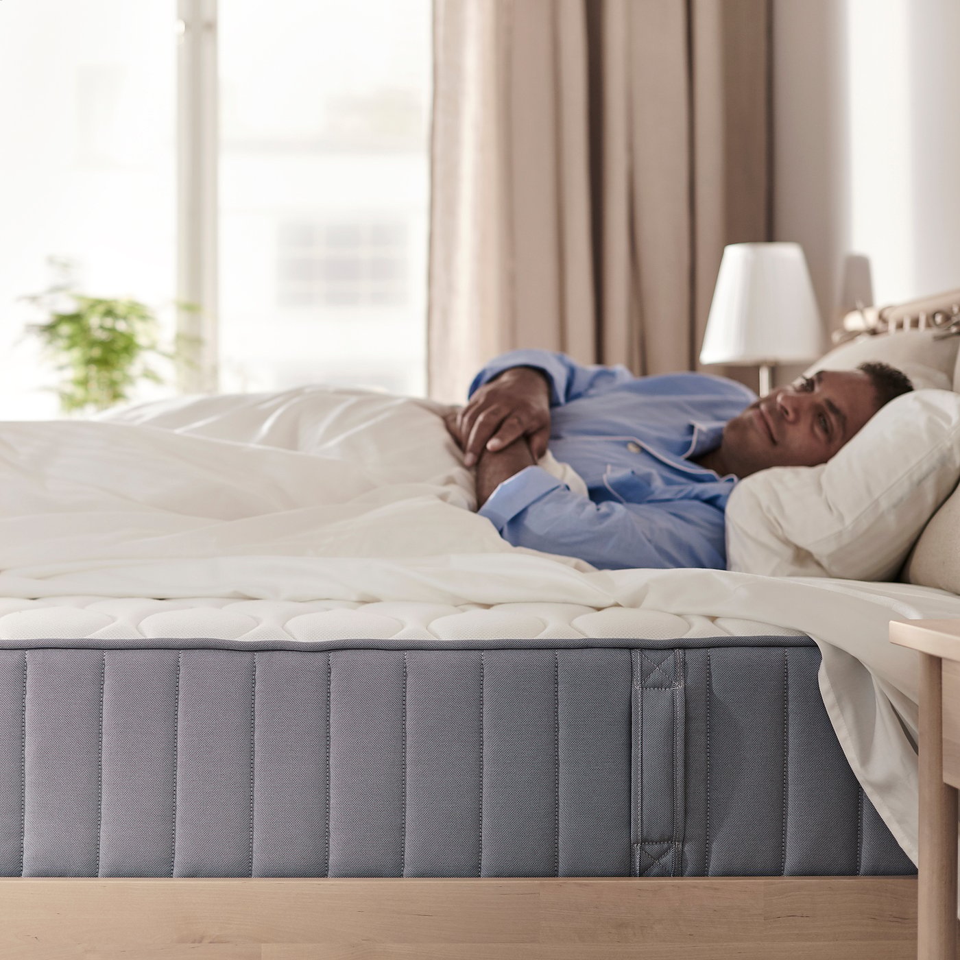 A person sleeping on a grey VÅGSTRANDA mattress on a white bed frame in a bedroom.