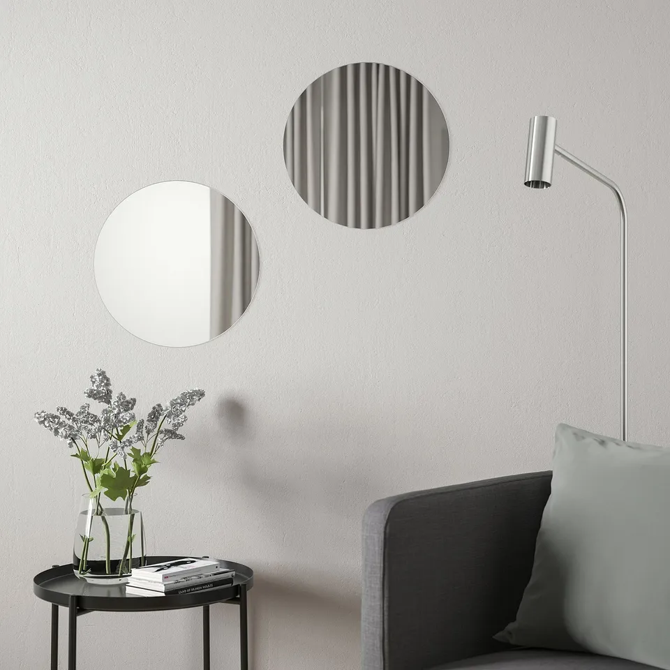 Minimalist decor: two BLÅSER mirrors above table with flowers, books, grey chair & lamp.