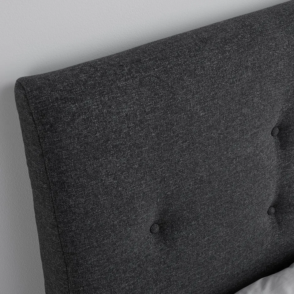 Close-up of a dark grey, upholstered headboard with button detailing, showcasing its soft, high-quality fabric.