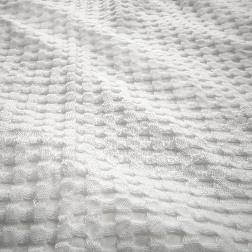 Close-up of white waffle-weave bedspread, textured cotton.