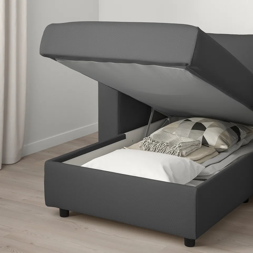 Grey sofa bed with open storage compartment revealing neatly folded blankets and pillows.