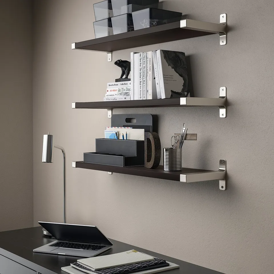 Wall-mounted shelves in a home office. Shelves hold books and office supplies. Laptop open on a desk below.