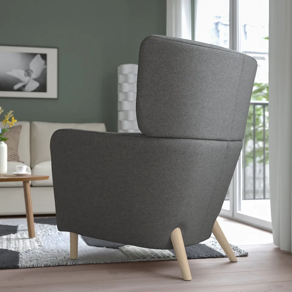 Grey wing chair by window, comfy & supportive, high back & wooden legs.