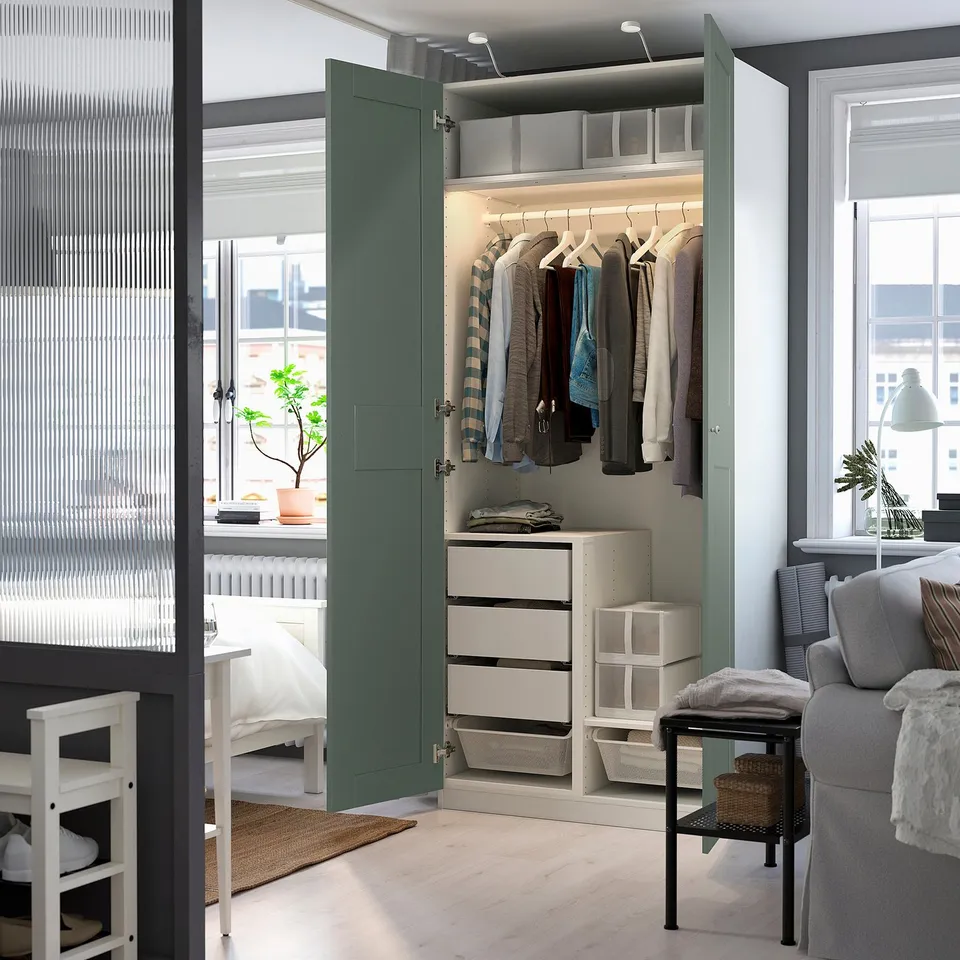 Open wardrobe with clothes, drawers, baskets, and interior lights in a simple, modern room.