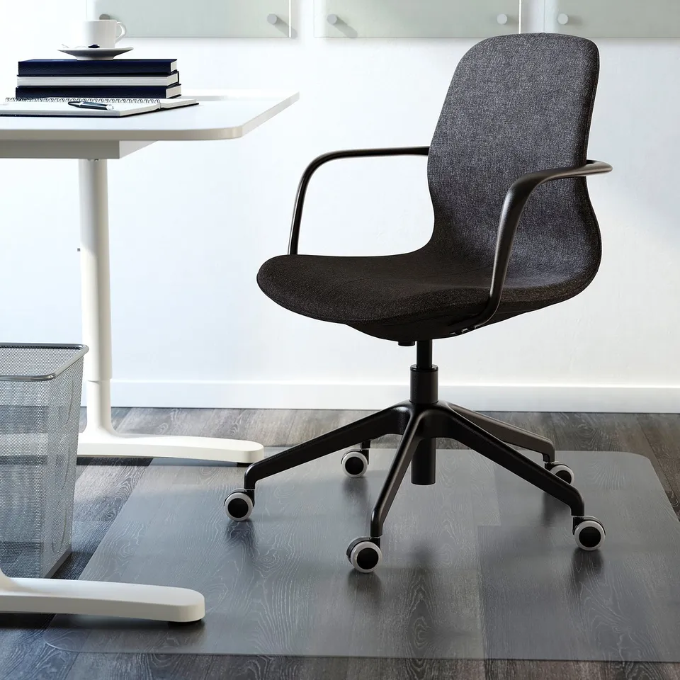 Modern black office chair with armrests and wheels under a white desk on a glass mat.